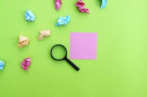 Top view photo of a magnifying glass and blank sticker on a green background.