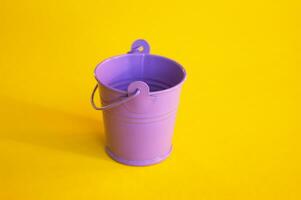 Miniature empty lilac bucket lies on a bright yellow background. photo