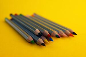 Many colorful pencils laying on yellow background. photo