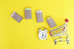 Shopping cart with paper bags and vintage clock on a yellow background. photo