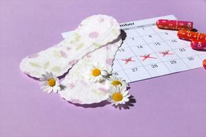 Menstrual pads and tampons on menstruation period calendar with chamomiles on pink background. photo