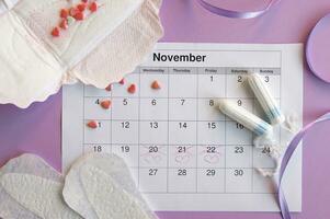 Menstrual pads and tampons on menstruation period calendar with on lilac background. photo