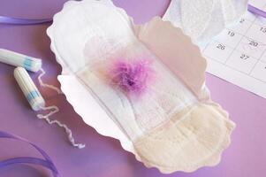 Menstrual pads and tampons on menstruation period calendar with on lilac background. photo