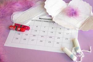 Menstrual pads and tampons on menstruation period calendar with on lilac background. photo