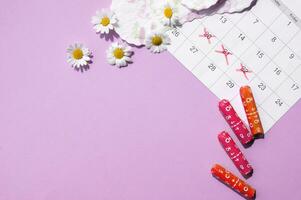 Menstrual pads and tampons on menstruation period calendar with chamomiles on pink background. photo