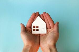 Hands holding white paper house in light blue background. photo