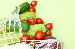 Ripe juicy red tomatoes, green cucumbers and zucchini in a string bag. photo