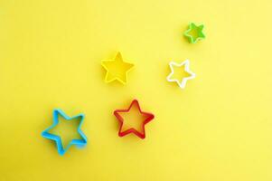 el plastico moldes de multi colores para haciendo galletas en el forma de un estrella en un amarillo antecedentes. foto