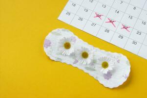 Menstrual pads with chamomiles on menstruation period calendar on yellow background. photo