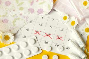 Menstrual pads and tampons on menstruation period calendar with chamomiles on yellow background. photo