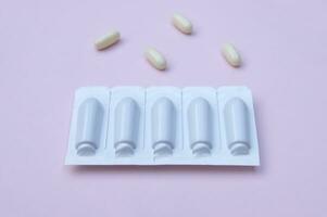 Gynecological medicines for women's health in form of suppository, capsules on pink background. photo