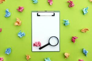 Magnifying glass, clipboard and crumpled colorful stickers around. photo