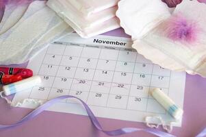 Menstrual pads and tampons on menstruation period calendar with on lilac background. photo