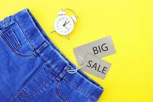 Flat lay, detail of jeans, grey labels and inscription Big Sale on yellow background. photo