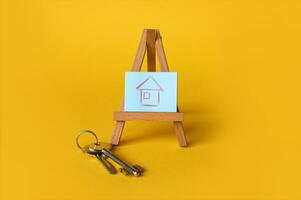 Drawing of a house on a wooden easel, nearby are the keys on a yellow background. photo