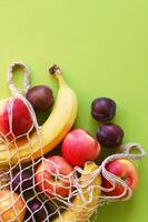 Red apples, bananas, plums and string bag on a bright green background. photo