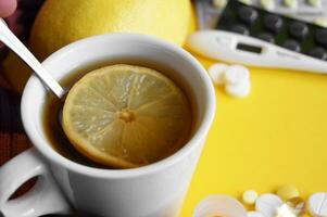 Cup of tea with lemon with pills and a thermometer on a yellow background. photo