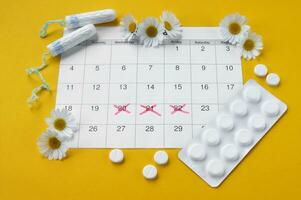 Menstrual pads and tampons on menstruation period calendar with chamomiles on yellow background. photo