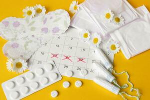 Menstrual pads and tampons on menstruation period calendar with chamomiles on yellow background. photo