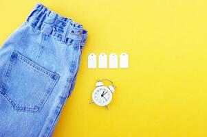 Flat lay, detail of jeans, blank white labels on yellow background. photo