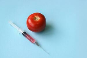 Tomato and syringe with GMO on a blue background. photo