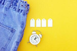 Flat lay, detail of jeans, blank white labels on yellow background. photo