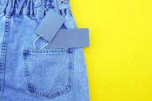 Flat lay, detail of blue jeans with blank gray label on yellow background. photo