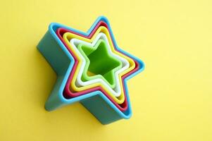 el plastico moldes de multi colores para haciendo galletas en el forma de un estrella en un amarillo antecedentes. foto