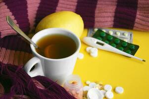 Cup of tea with lemon with pills and a thermometer on a yellow background. photo