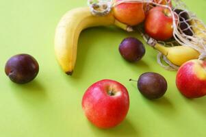 rojo manzanas, plátanos, ciruelas y cuerda bolso en un brillante verde antecedentes. foto