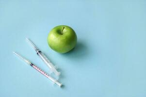 Green apple and syringe with GMO on a blue background. photo