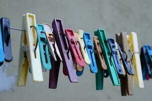 Multi-colored clothespins hang on a wire against the gray wall. photo