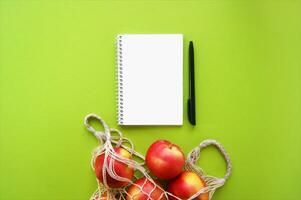 rojo manzana en cuerda bolso y cuaderno con bolígrafo en un brillante verde antecedentes. foto