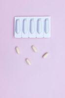 Gynecological medicines for women's health in form of suppository, capsules on pink background. photo