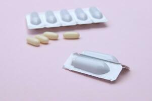Gynecological medicines for women's health in form of suppository, capsules on pink background. photo