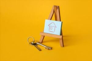 Drawing of a house on a wooden easel, nearby are the keys on a yellow background. photo