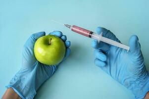 Green apple and syringe with GMO in hands on a blue background. photo