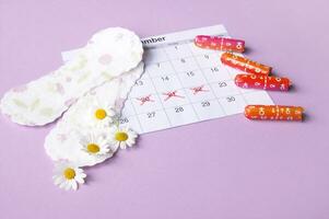 Menstrual pads and tampons on menstruation period calendar with chamomiles on pink background. photo