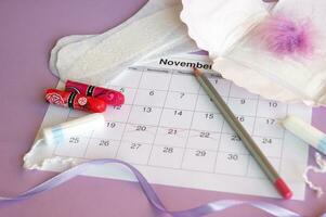 Menstrual pads and tampons on menstruation period calendar with on lilac background. photo