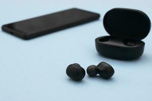 Smartphone and wireless headphones or earbuds with charging case on bright blue background. photo
