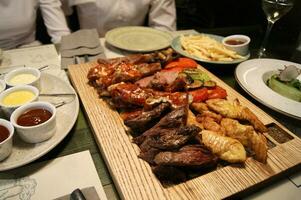 Table with a board of various cooked meat, salads and sauces photo