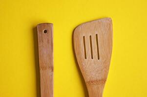 Top view of wooden kitchen spoon and spatula isolated on yellow background. photo