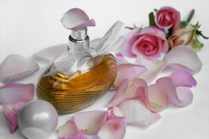 Perfume bottle with rose petals and pearls on a light background. photo