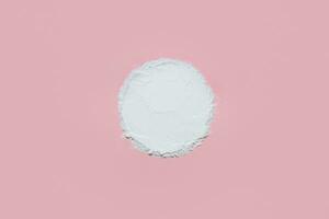 White face powder with empty circle inside on pink background photo