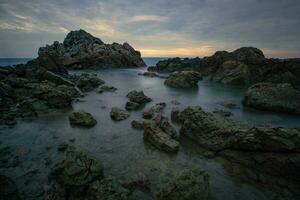 rocoso playa con rocas y agua a amanecer foto