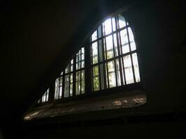 Big arched window with double frame and light shining through it, photograph taken from a dark room bottom up view photo