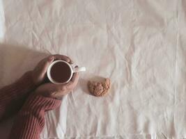 hand holding tea cup, cookie on table, cozy hugge concept. Pastel colors, warm sweater, vintage style. High quality photo. photo