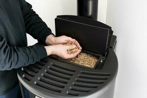 Pellet stove, man holding granules in his hand above a modern black stove photo