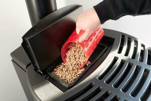 Close-up on pellets, black domestic pellet stove, man loading by hand granules with a red 3 d printed cup photo