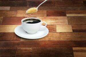 Spoon of sugar poured into a coffee mug with a white saucer on a wooden background. photo